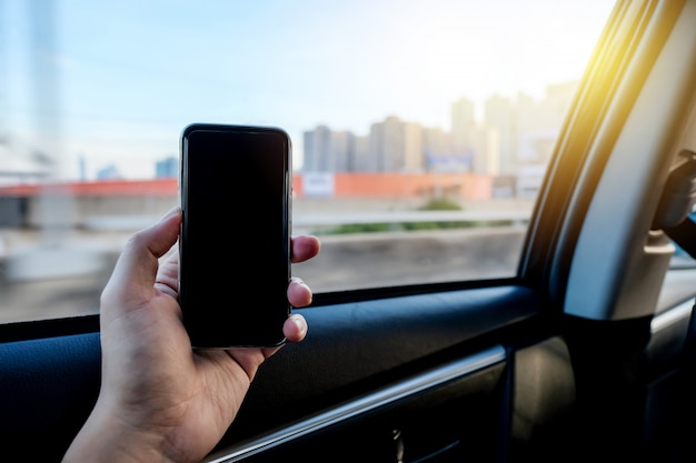 Mano agarrando teléfono inteligente para utilizar la aplicación móvil en el asiento trasero del coche de taxi.