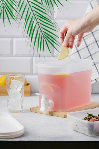 Una mano agrega una rodaja de limón a una bebida refrescante rosa en un luminoso interior de cocina