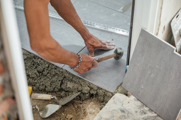 Mano del alicatador colocando y usando un mazo golpeando baldosas de granito en el piso