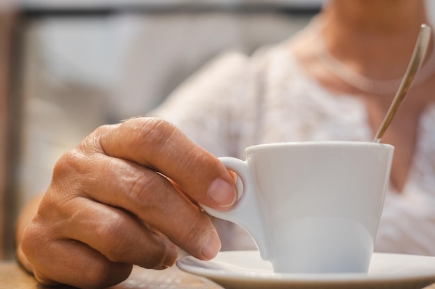 Mano de anciana sosteniendo una taza blanca de tiempo de descanso para café espresso con bebida caliente aromática