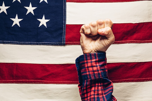 Foto mano apretada en puño contra la bandera estadounidense. fuerza, poder y confiabilidad del concepto de ee.uu. y el día del trabajo