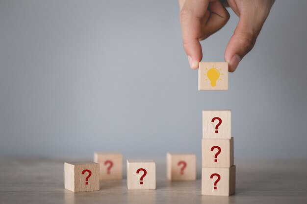 Mano arreglando el apilamiento de bloques de madera con icono de signo de interrogación y lámpara, pensando con el concepto de signo de interrogación