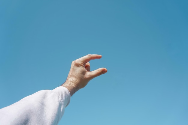 mano arriba en el aire gesticulando en el cielo azul, fondo azul