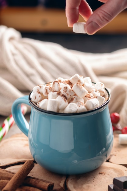 Mano arroja malvaviscos en una taza de chocolate caliente.