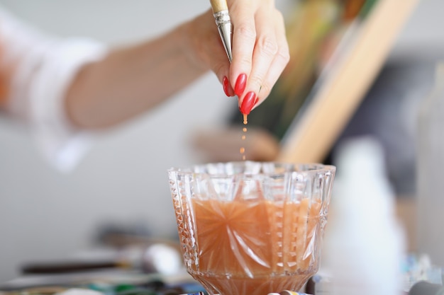 La mano de un artista con una manicura saca un pincel de un vaso de agua la orientación familiar