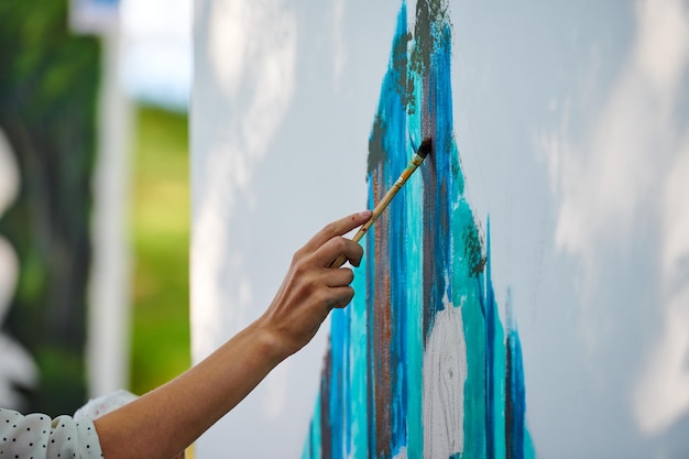 La mano del artista sostiene un pincel y dibuja una imagen surrealista abstracta en un lienzo blanco en un festival al aire libre