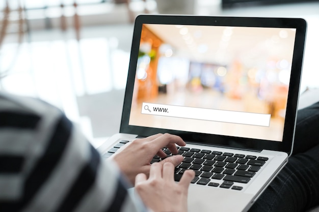 Foto mano atando la computadora labtop con www. en la barra de búsqueda sobre fondo borroso de la tienda en la pantalla