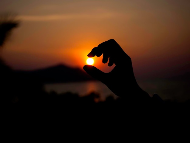 Una mano atrapa el sol La silueta del primer plano extiende la mano sosteniendo un sol en el cielo del atardecer