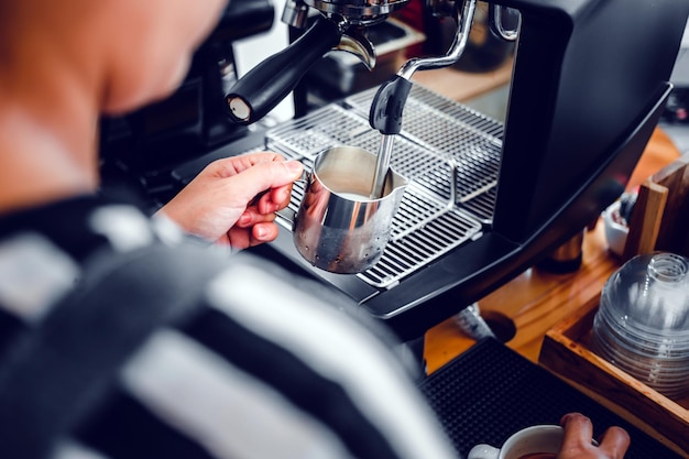 Mano de un barista en la cafetería preparando y usando una máquina de café para vaporizar leche para un café