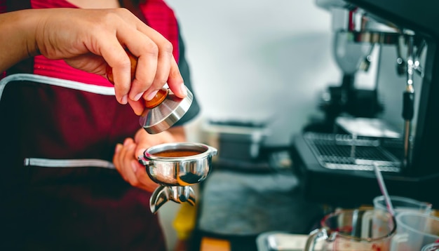 Mano de un barista sosteniendo un portafiltro y un manipulador de café haciendo un café expreso