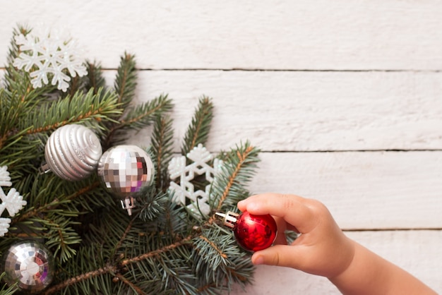 Mano de bebé y árbol de Navidad con decoración sobre fondo de madera blanca, espacio de copia. vacaciones de invierno para niños