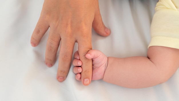 Mano de bebé y dedo de adulto sobre fondo de cama de sábana blanca