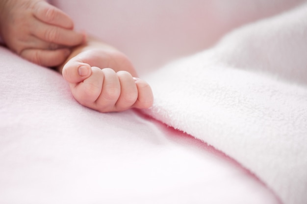 Mano del bebé recién nacido en manta rosa en tono de color suave
