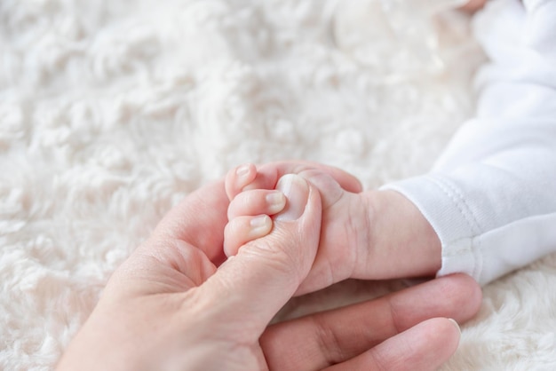Mano de bebé recién nacido sosteniendo el dedo de mamá en la cama