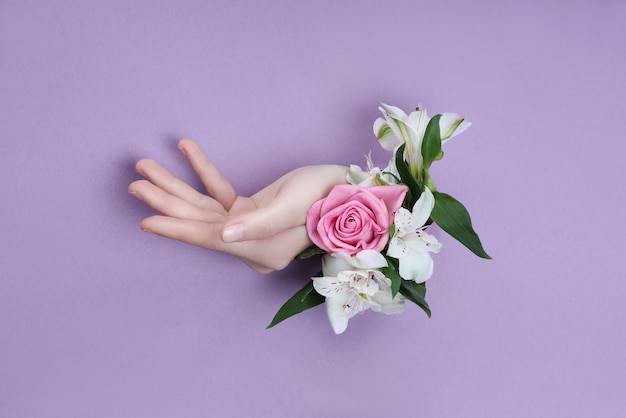 Mano de belleza con flores en un agujero en un fondo de papel morado. Nature Hand Cosmetics, extracto de flor natural, hidratante y suavizante de la piel.