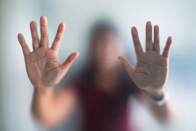 Mano borrosa de la mujer detrás del pánico de vidrio esmerilado, pánico y negativo oscuro emocional