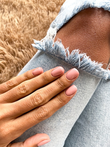 Mano bronceada de una mujer con una suave manicura rosa-beige, cubierta con esmalte en gel