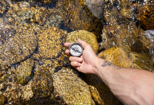 Mano con una brújula cerca del río.