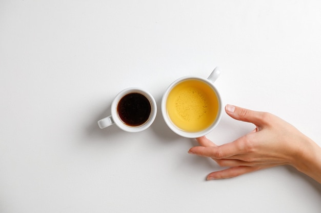 Mano con café frente al té. Taza de café negro frente a la taza de té verde sobre una mesa blanca con la mano. Minimalismo.