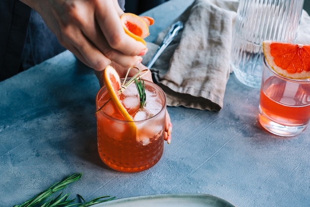 La mano del camarero exprime el jugo de toronja fresca en limonada cóctel con hielo y romero.