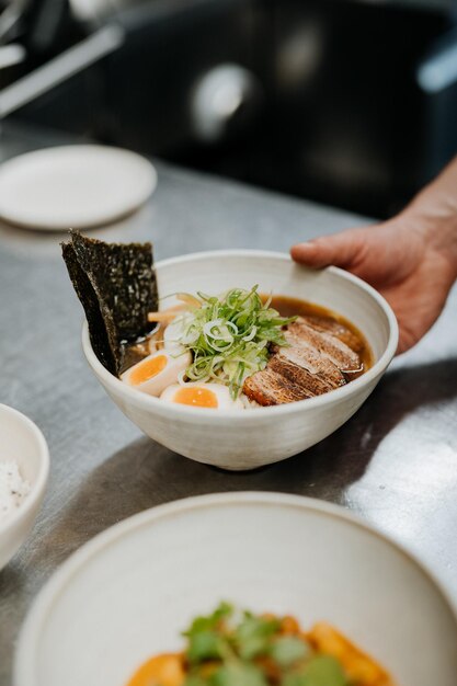 Mano de camarero irreconocible que sirve ramen de sopa de fideos asiáticos con carne tofu verduras nori y huevo