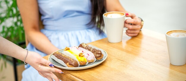 Mano de camarero pone un plato con canutillos sobre la mesa de madera para mujer joven bebiendo café en un café