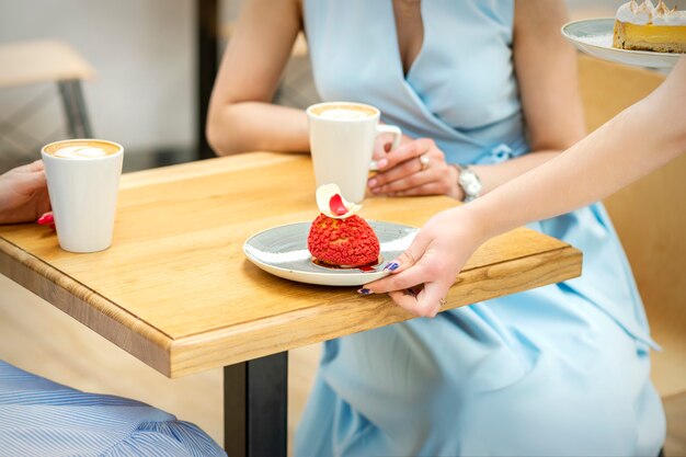 La mano del camarero pone sobre la mesa un plato con un cupcake rojo en el fondo de una clienta en un café