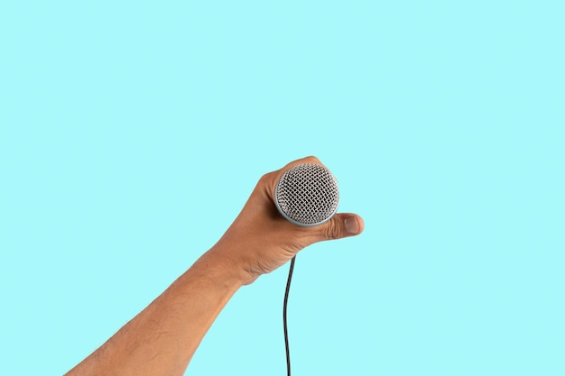 Foto la mano del cantante masculino negro sosteniendo un micrófono aislado sobre un fondo cian