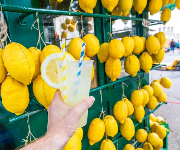 Foto mano caucásica con limonada fresca y saludable durante el fondo de limones de verano