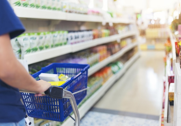 Mano de cerca de una compradora con un carrito de compras en un supermercado con luz bokeh desfocada