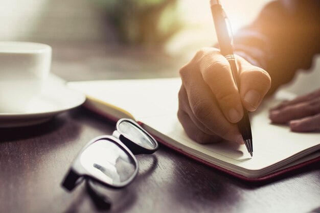 mano de cerca de personas que usan vaqueros escribiendo diario y nota información en la mesa de trabajo en casa