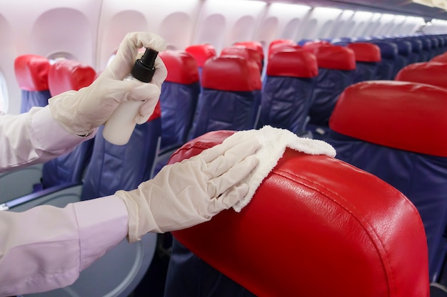 La mano cercana lleva guantes limpiando el asiento del avión para la pandemia de prevención covid-19