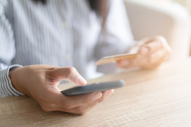 Una mano cercana de mujeres asiáticas está comprando en línea con una tarjeta de crédito. Las mujeres están usando un teléfono inteligente y haciendo transacciones en línea. Concepto de compras en la tienda en línea y entrega rápida.