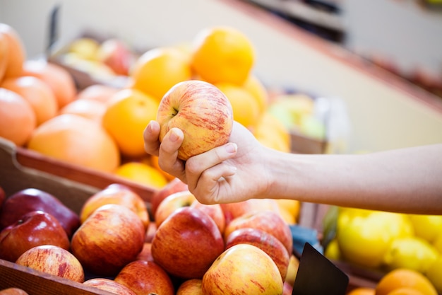 La mano cerrada selecciona manzanas en el estante de la tienda de verduras.