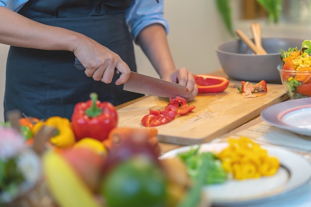 Mano de chef de primer plano cortar el pimiento en la tabla de cortar en la cocina moderna