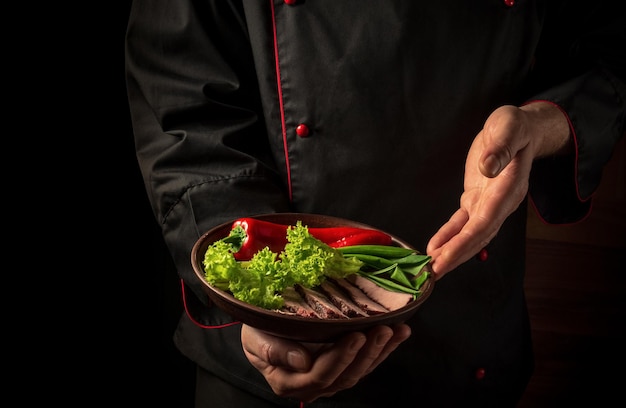 En la mano de un chef profesional hay un plato con bistec picado y verduras