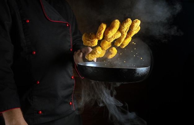 La mano de un chef profesional lanza nagits en una sartén caliente con vapor sobre un fondo negro El concepto de cocinar en el hotel Espacio publicitario gratuito