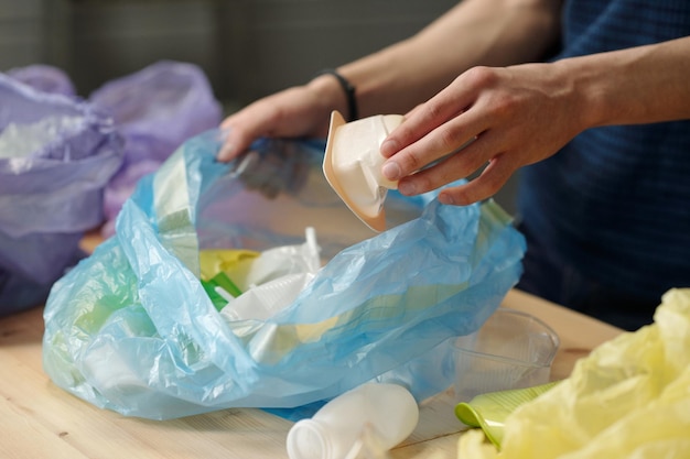 Mano de chico adolescente poniendo un pequeño recipiente de yogur de plástico blanco en un saco