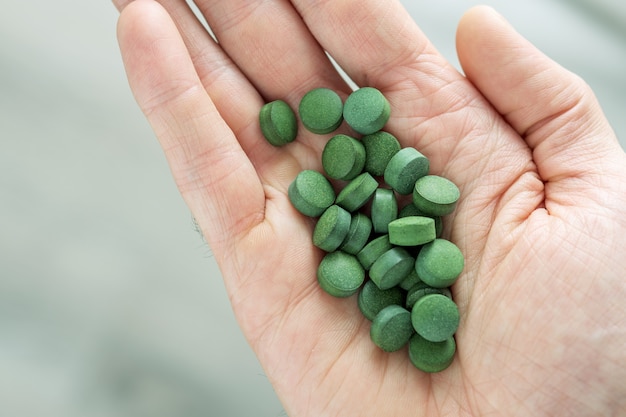 Mano con chlorella o tabletas de espirulina sobre fondo gris. Vista superior.