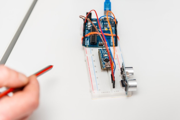Una mano de científicos Sensor de distancia ultrasónico Arduino Nano placa ultrasónica Proyectos de estambre y mini proyectos de ingeniería Componentes de construcción colocados planos sobre una mesa blanca