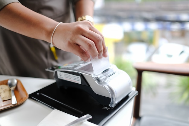 Mano del cliente que paga con tarjeta de crédito sin contacto con tecnología NFC. Camarero con una máquina de lector de tarjetas de crédito en barra de bar con tarjeta de crédito femenina. Centrarse en las manos.