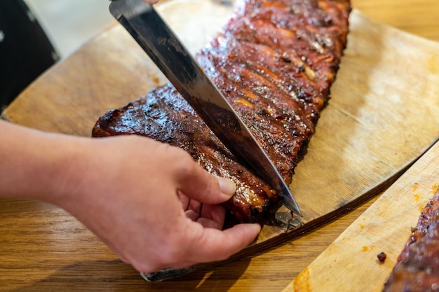 La mano del cocinero cortó sabrosas costillas de cerdo ahumadas en un escritorio de madera