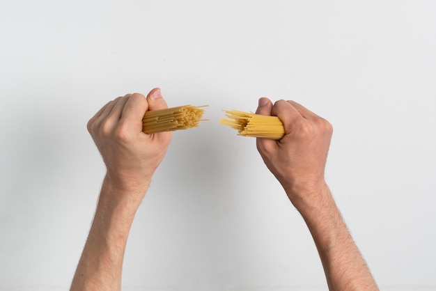 La mano del cocinero rompe la pasta de espagueti cruda italiana antes de la preparación