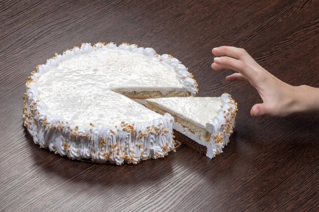 La mano codiciosa agarra un trozo de un gran pastel blanco con una tapa en blanco