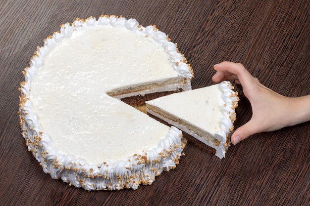 La mano codiciosa agarra un trozo de un gran pastel blanco con una tapa en blanco