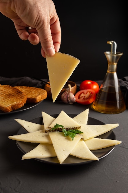 Mano cogiendo una loncha de queso. mesa rústica oscura