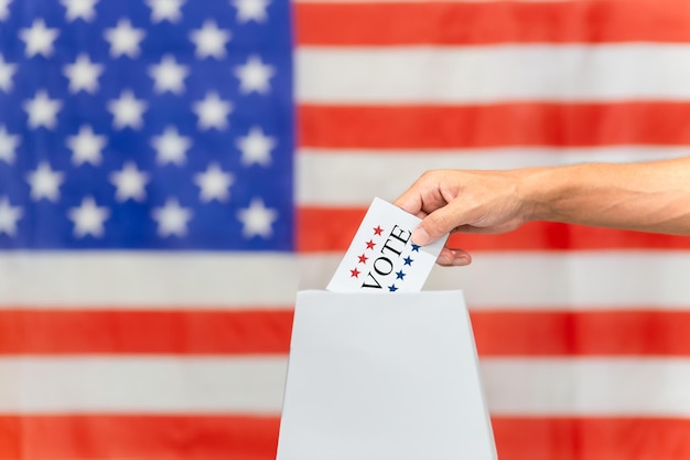 mano colocando una boleta en la caja de votación con fondo de la bandera de los Estados Unidos