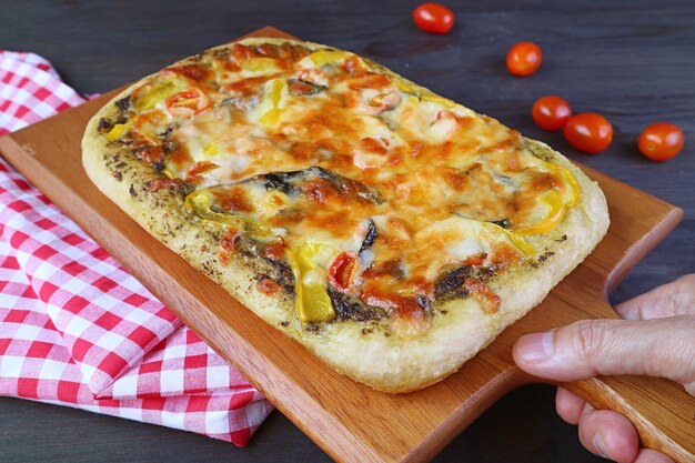 Mano colocando deliciosa pizza vegetariana al pesto casera recién horneada sobre la mesa