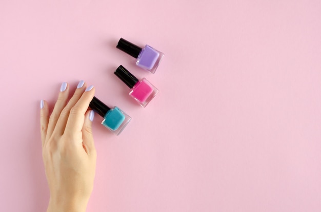 Foto mano con composición de esmalte de uñas de color sobre fondo rosa.