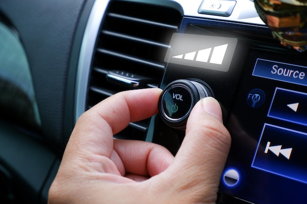 La mano del conductor ajusta el control de volumen en el salpicadero de la radio del coche